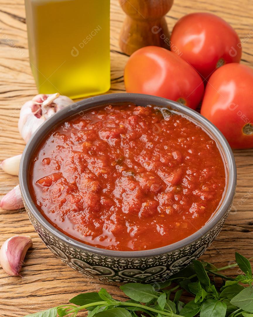 Molho de tomate, tomate, alho, azeite e ervas sobre a mesa de madeira.