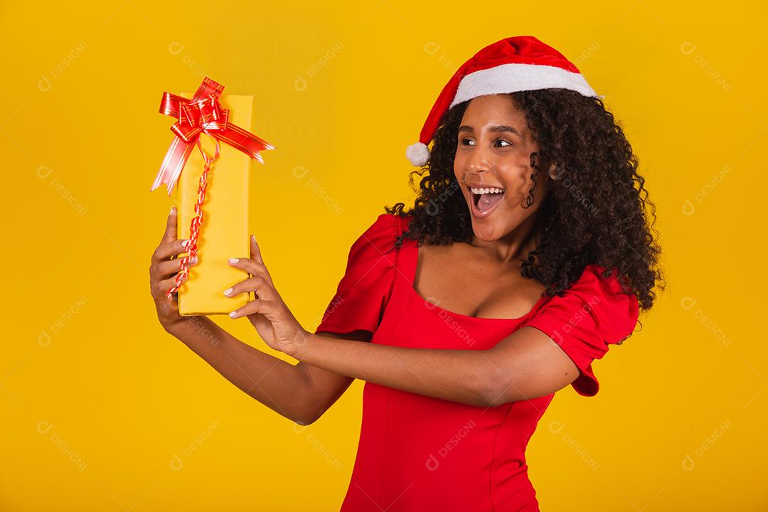 Jovem afro segurando um presente de Natal expressivo.