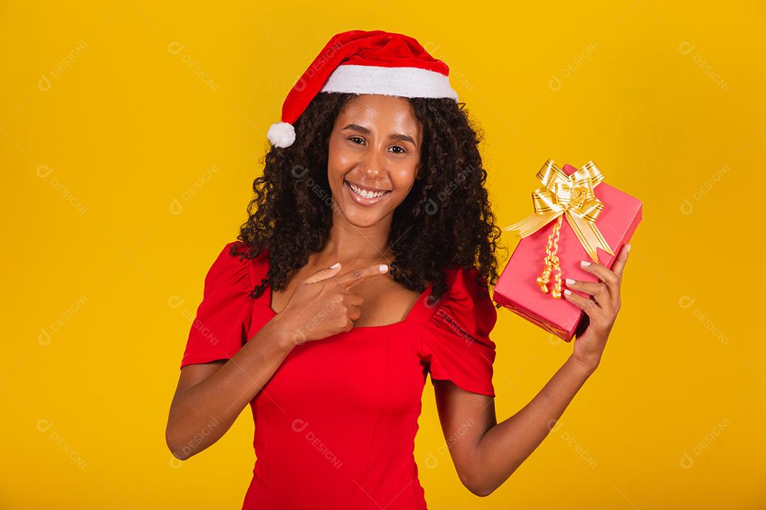 Linda garota afro com seu presente de natal apontando para ele