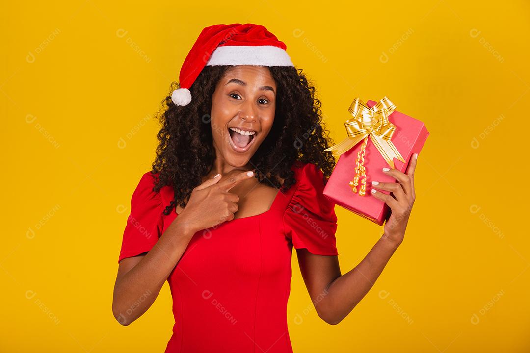 Linda garota afro com seu presente de natal apontando para ele
