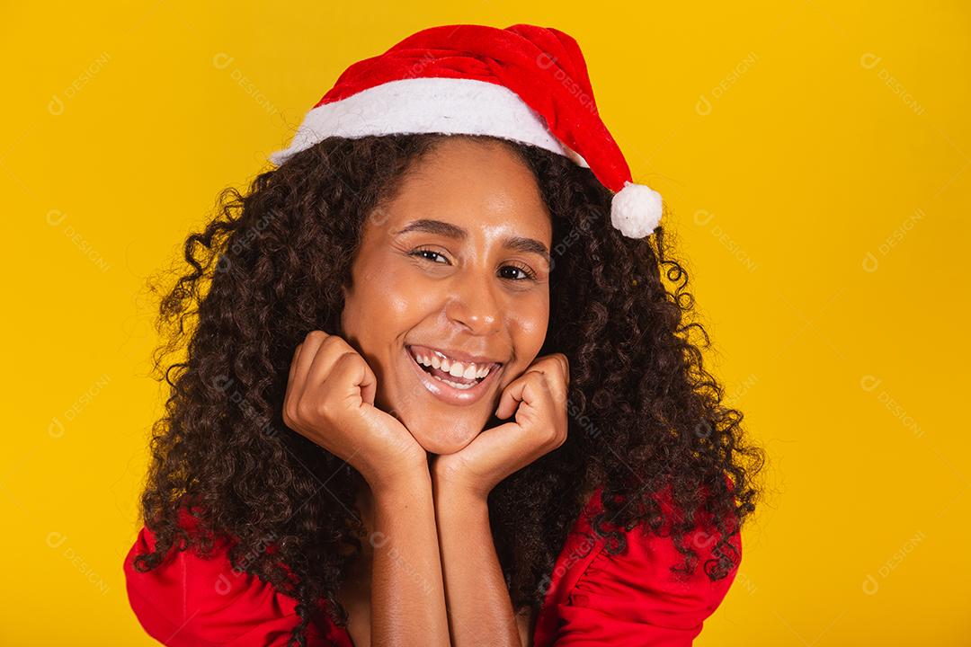 Mulher afro sorridente com chapéu de papai noel sorrindo para a câmera