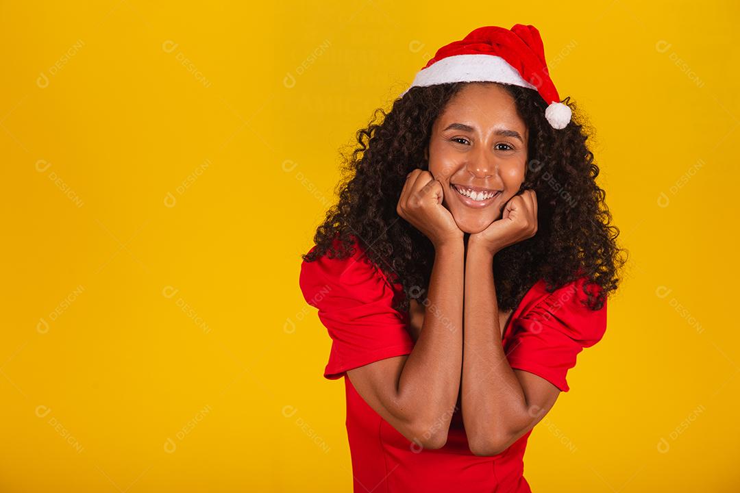 Mulher afro sorridente com chapéu de papai noel sorrindo para a câmera