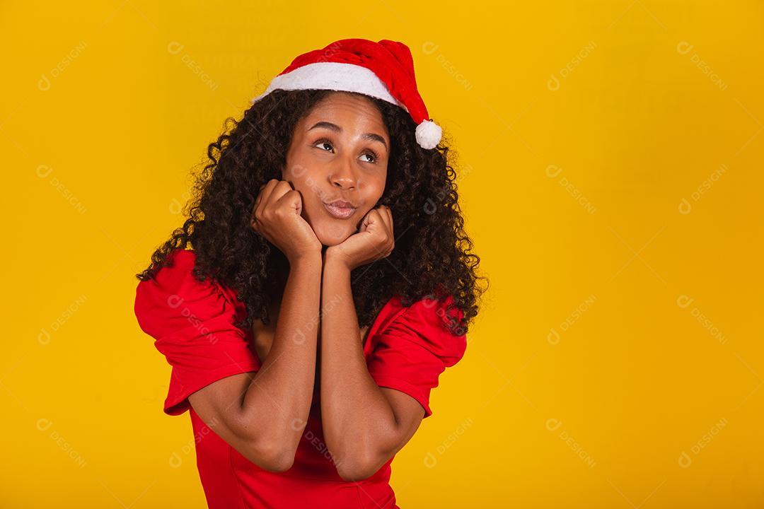 Mulher afro sorridente com chapéu de papai noel sorrindo para a câmera