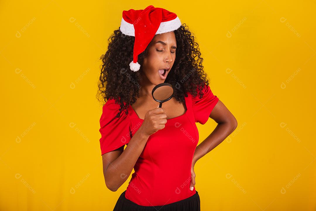 mulher vestida para o natal com chapéu de papai noel usando uma lupa
