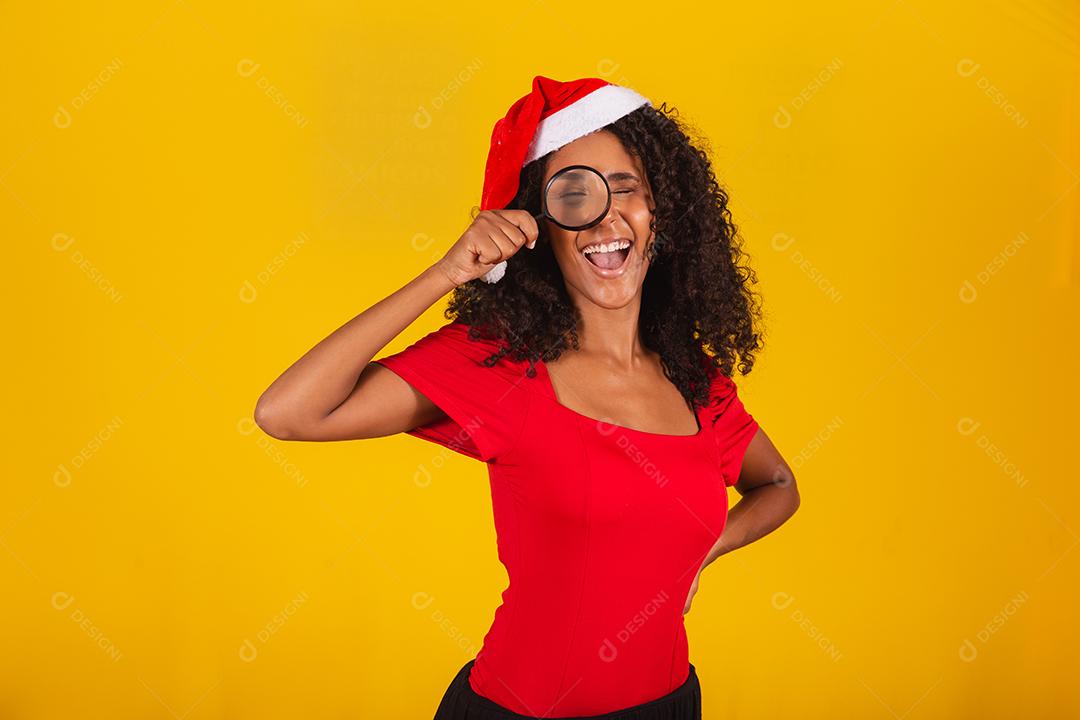 mulher vestida para o natal com chapéu de papai noel usando uma lupa