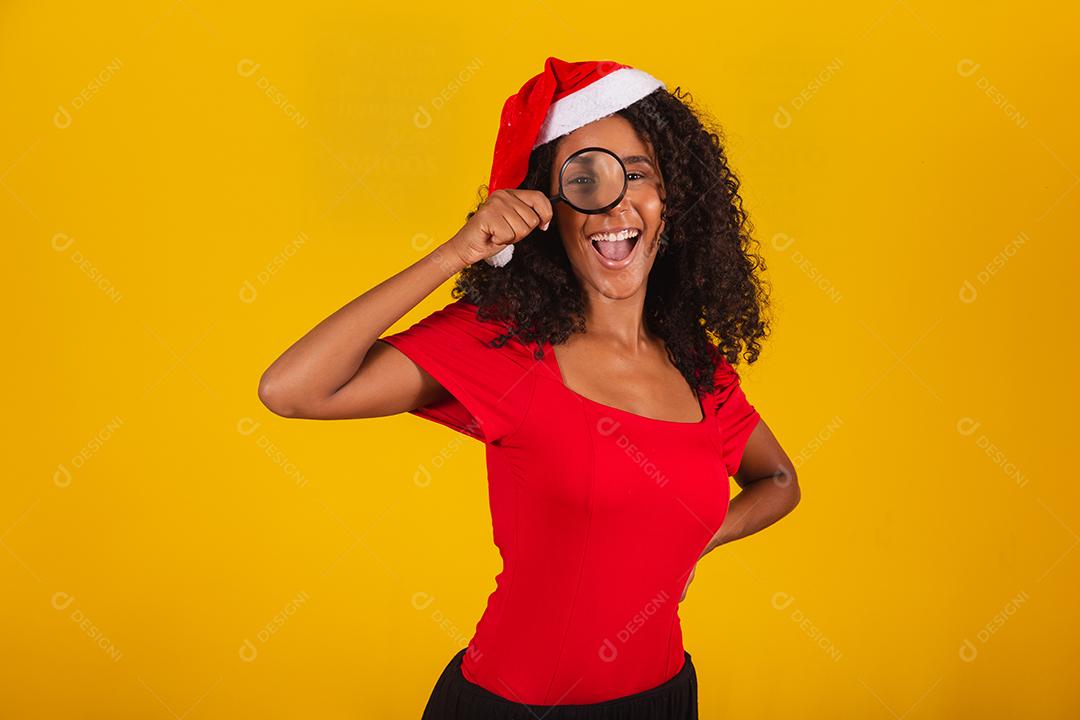 mulher vestida para o natal com chapéu de papai noel usando uma lupa