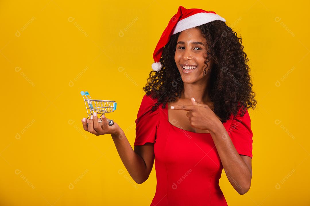 MulherMulher de chapéu de Papai Noel fazendo compras de Natal. Ela está mostrando um mini carrinho
