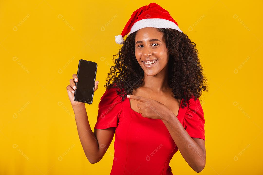 Sorrindo jovem Santa no chapéu de Natal segurando o celular com tela em branco vazia isolada em fundo amarelo.