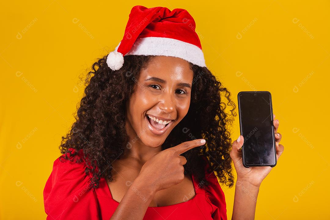 Sorrindo jovem Santa no chapéu de Natal segurando o celular com tela em branco vazia isolada em fundo amarelo.