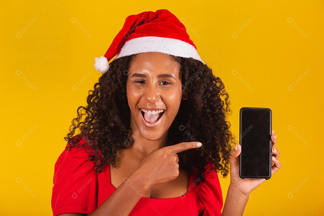 Sorrindo jovem Santa no chapéu de Natal segurando o celular com tela em branco vazia isolada em fundo amarelo.