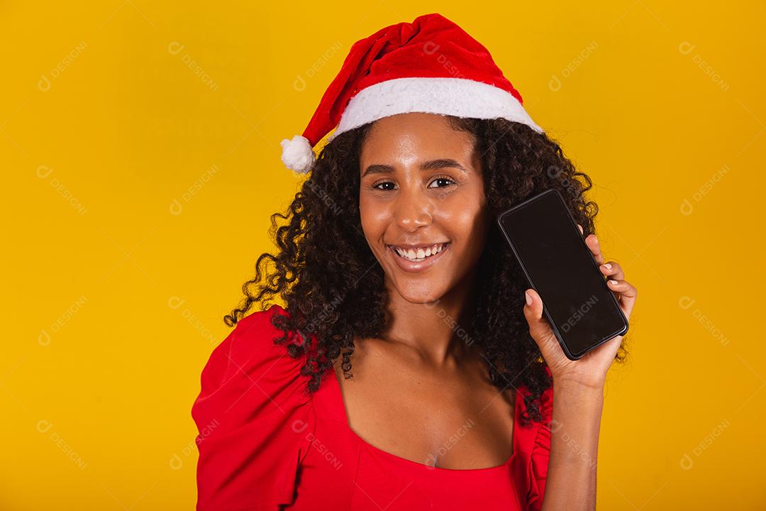 Sorrindo jovem Santa no chapéu de Natal segurando o celular com tela em branco vazia isolada em fundo amarelo.