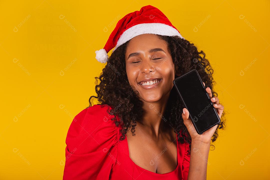Sorrindo jovem Santa no chapéu de Natal segurando o celular com tela em branco vazia isolada em fundo amarelo.