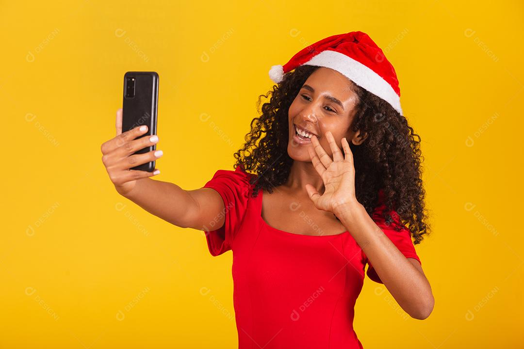 Sorrindo jovem Santa no chapéu de Natal segurando o celular com tela em branco vazia isolada em fundo amarelo.
