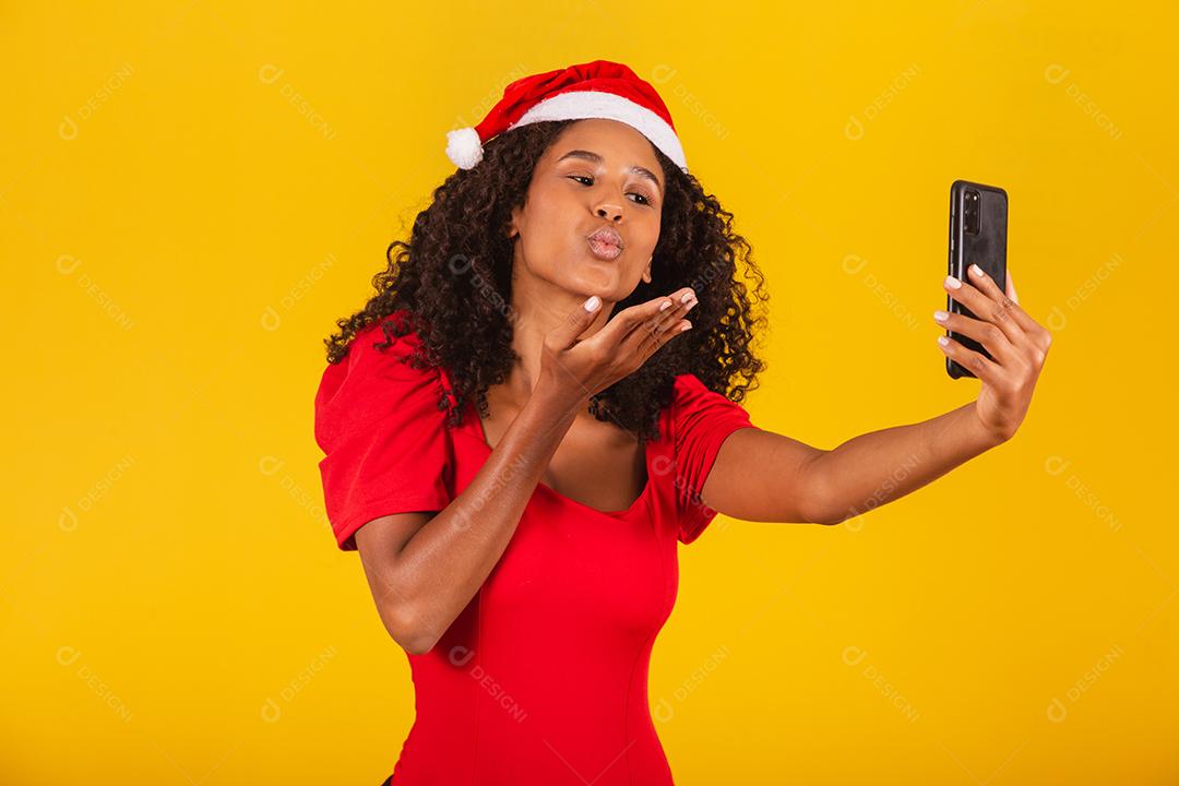 Sorrindo jovem Santa no chapéu de Natal segurando o celular com tela em branco vazia isolada em fundo amarelo.