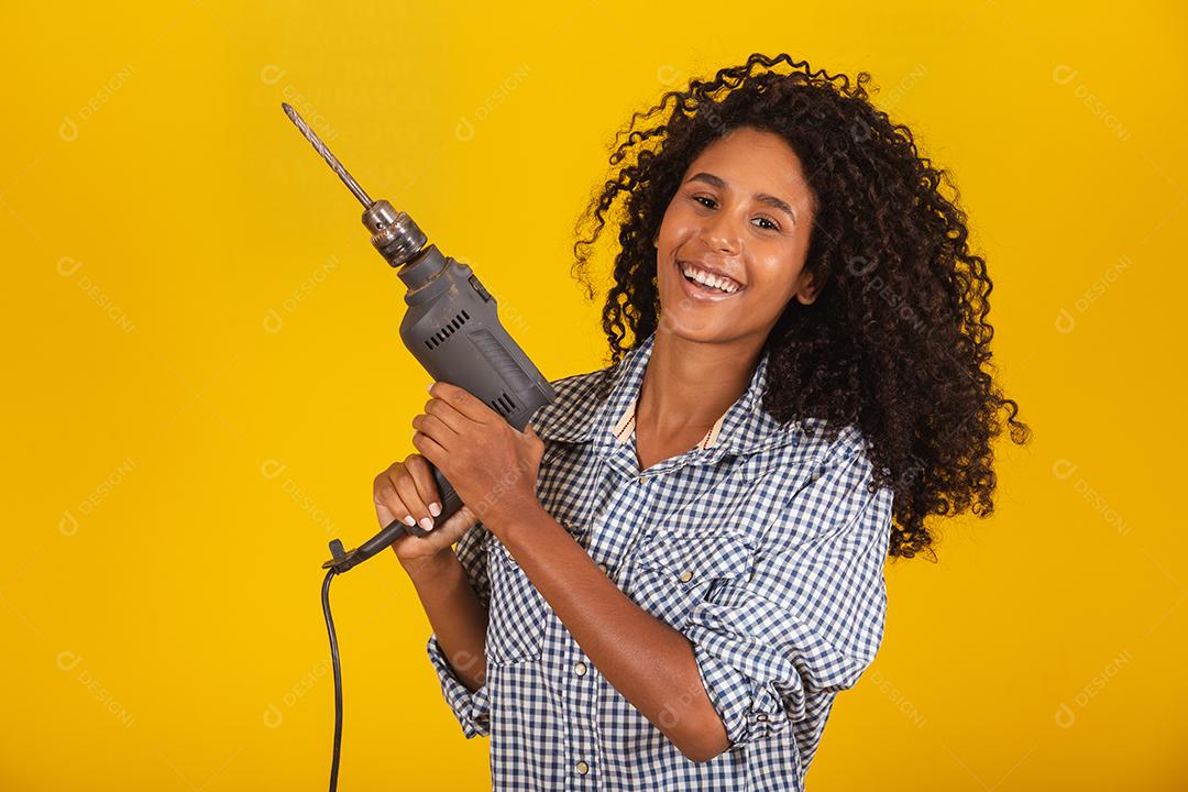Mulher empreiteira com uma broca em fundo amarelo.