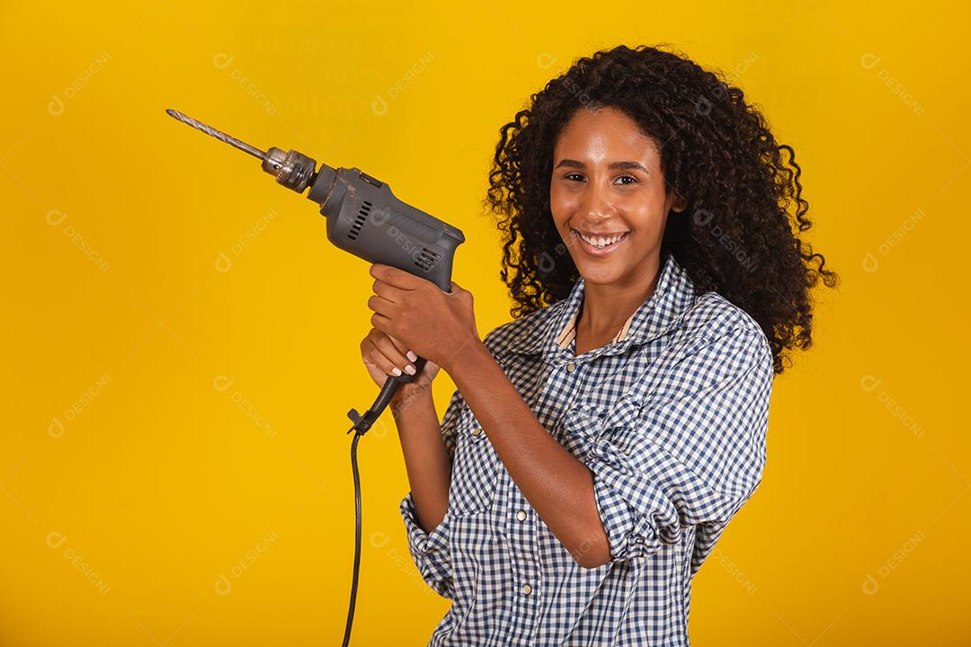 Mulher empreiteira com uma broca em fundo amarelo.