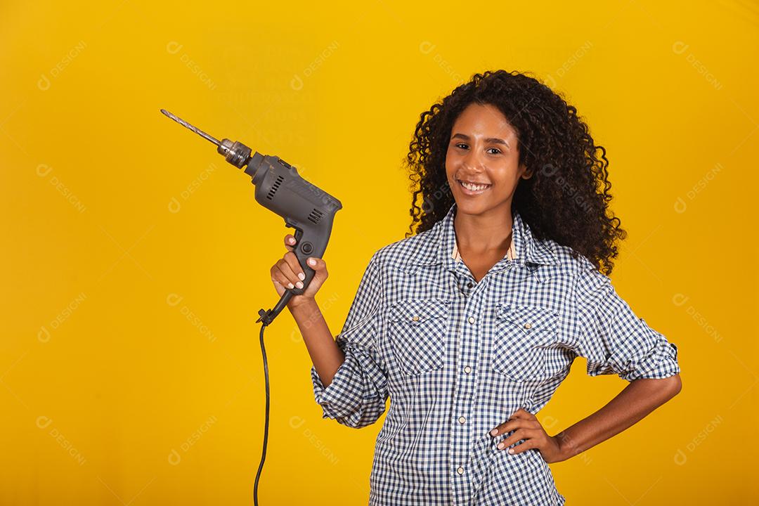 Mulher empreiteira com uma broca em fundo amarelo.