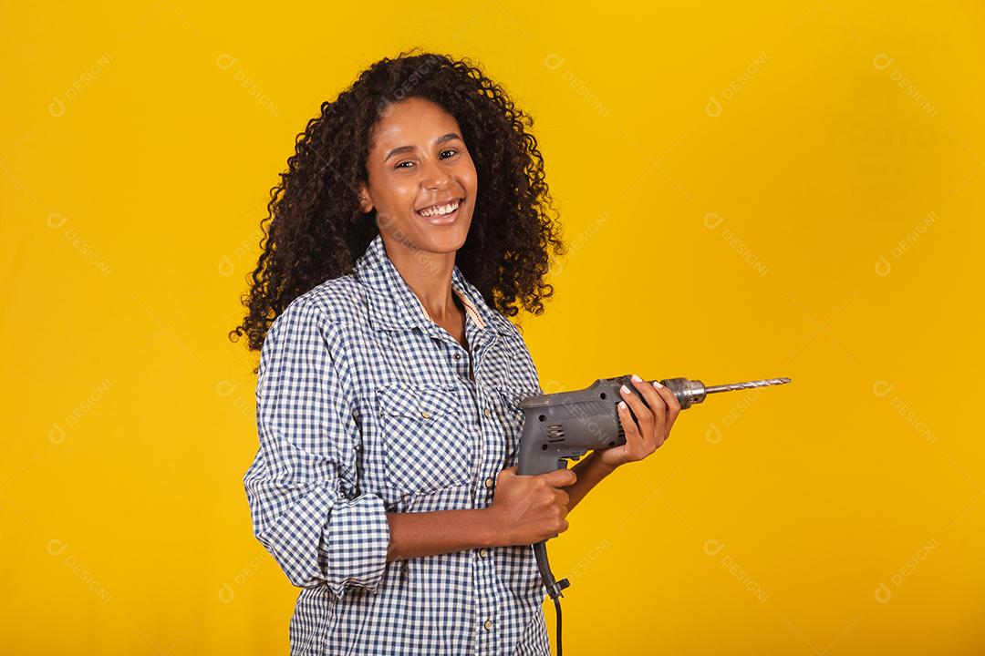 Mulher empreiteira com uma broca em fundo amarelo.