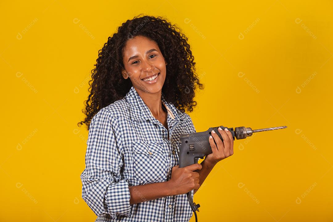 Mulher empreiteira com uma broca em fundo amarelo.