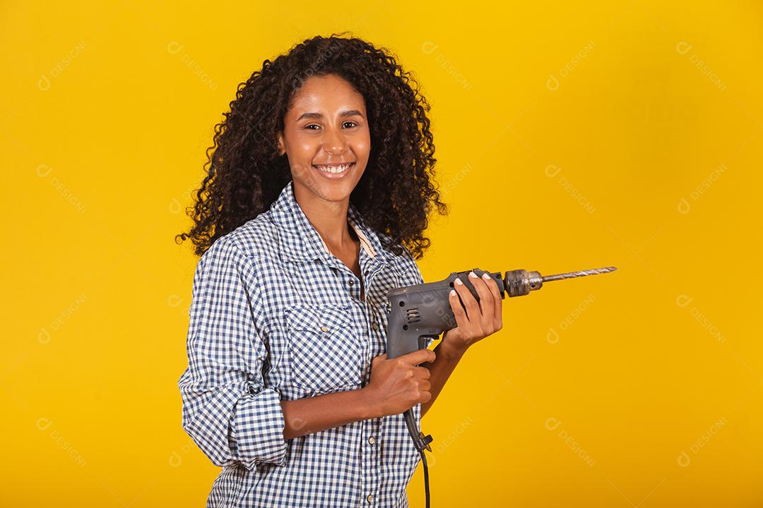 Mulher empreiteira com uma broca em fundo amarelo.