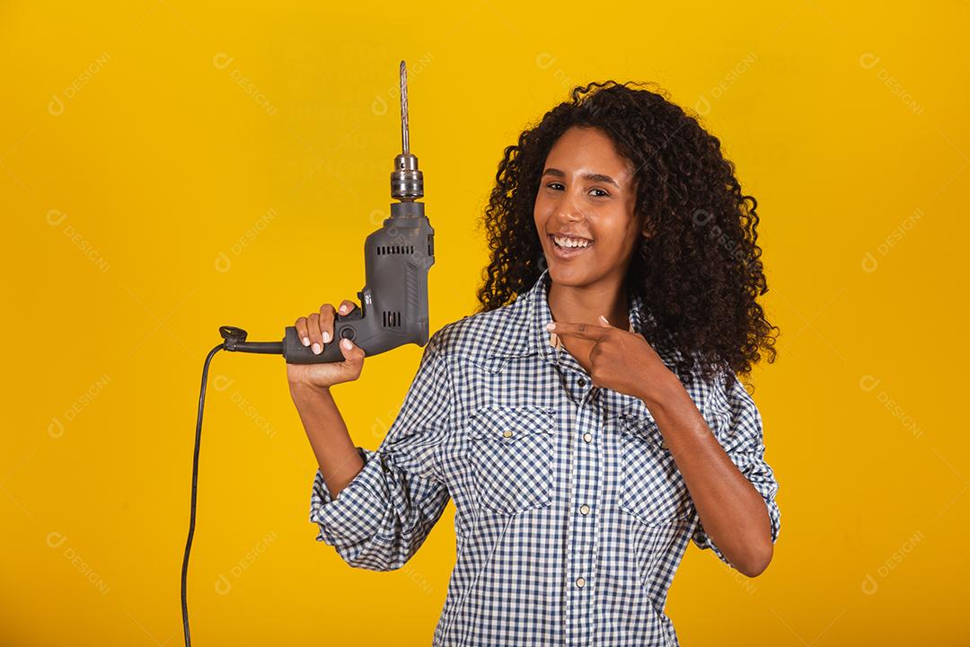 Mulher empreiteira com uma broca em fundo amarelo.