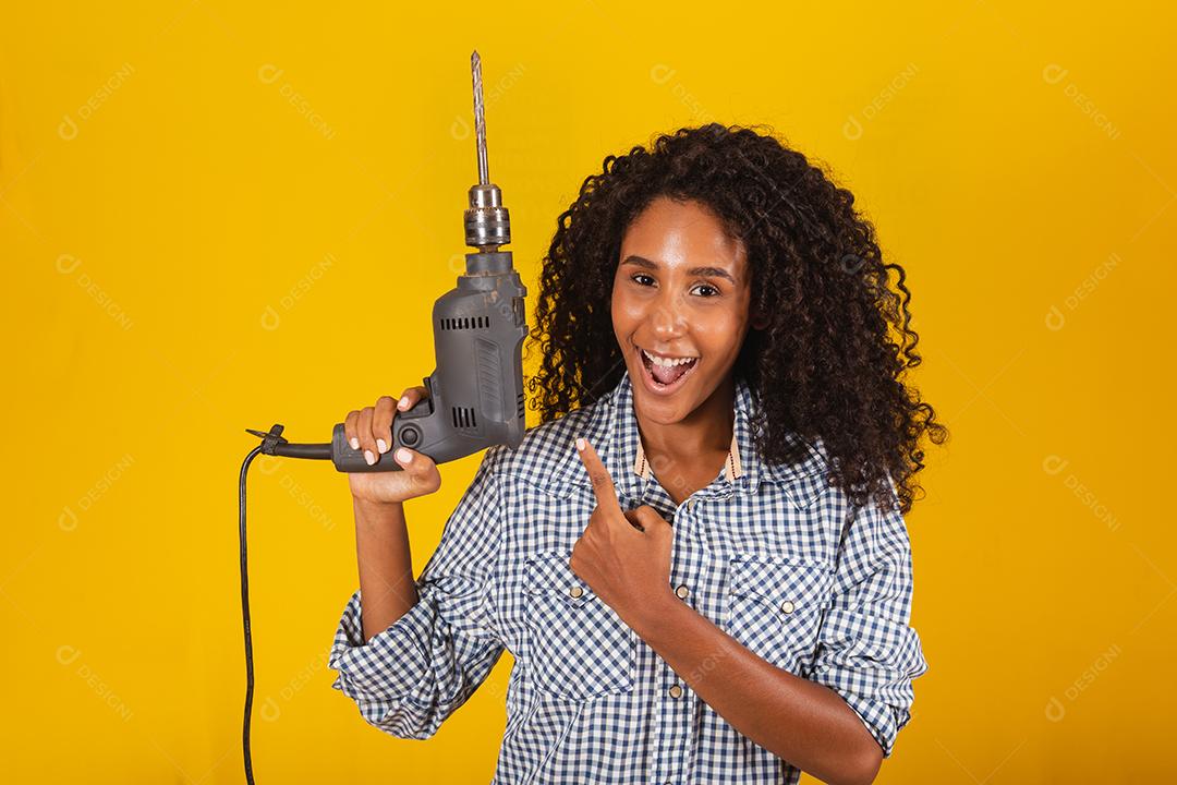 Mulher empreiteira com uma broca em fundo amarelo.