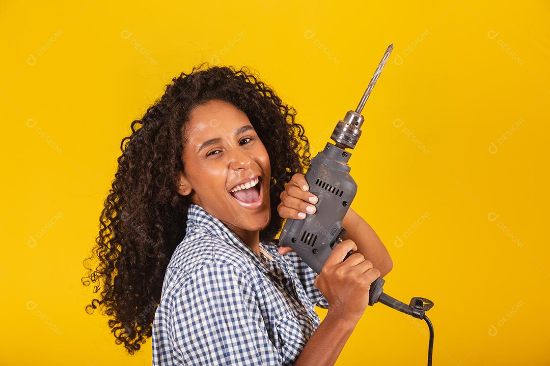 Mulher empreiteira com uma broca em fundo amarelo.