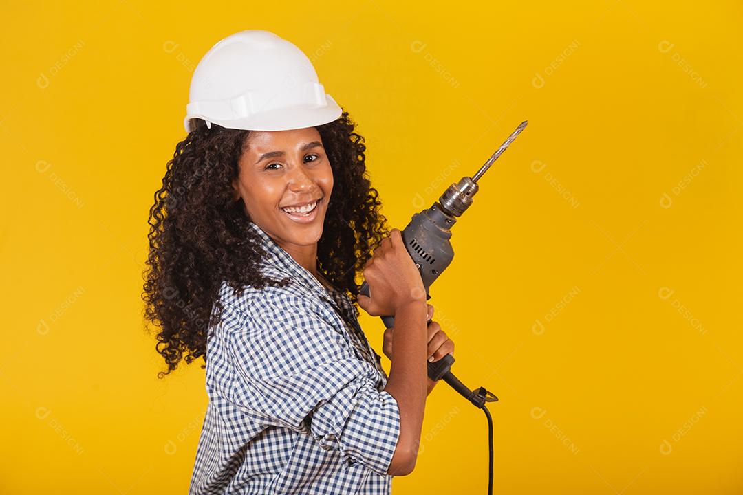 Mulher empreiteira com uma broca em fundo amarelo.