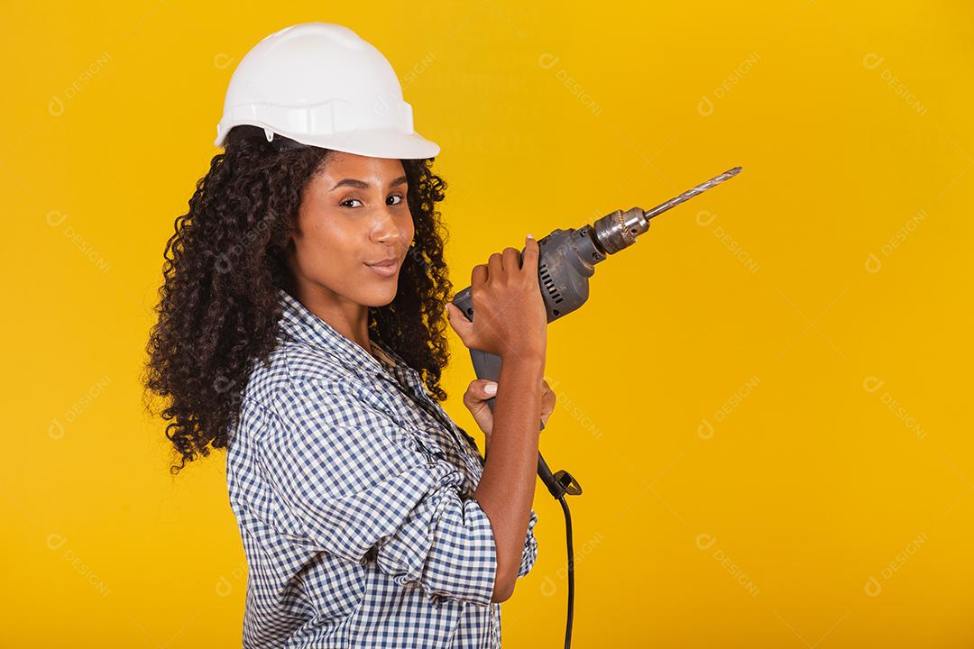 Mulher empreiteira com uma broca em fundo amarelo.