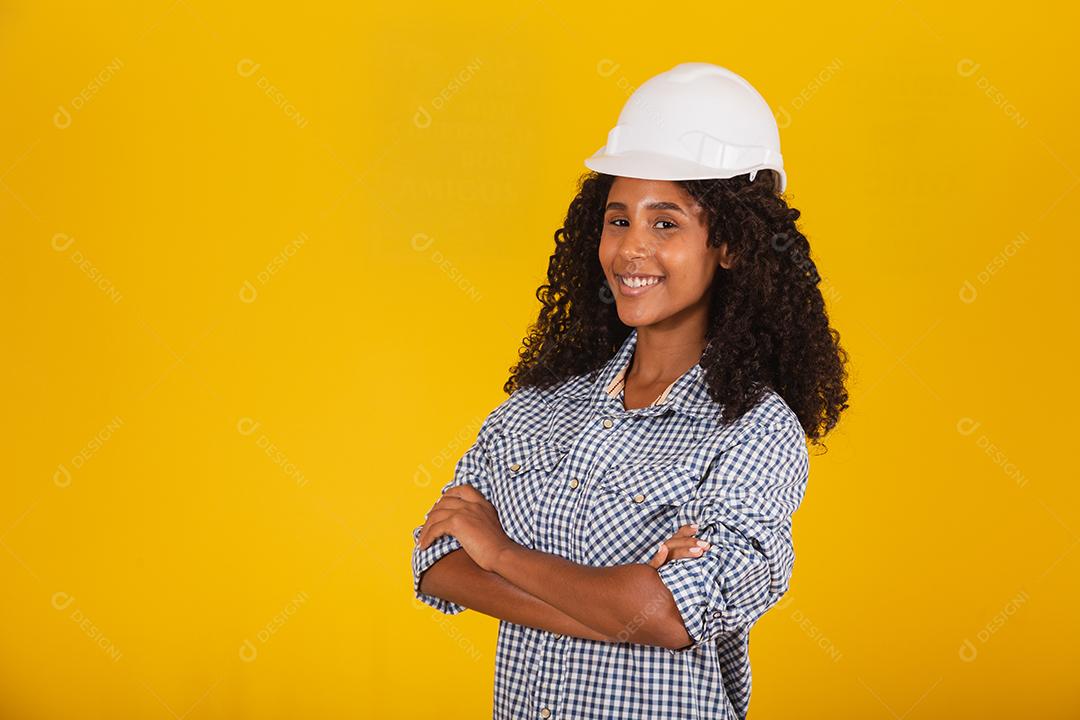 Engenheira ou arquiteta em fundo amarelo sorrindo com os braços cruzados.