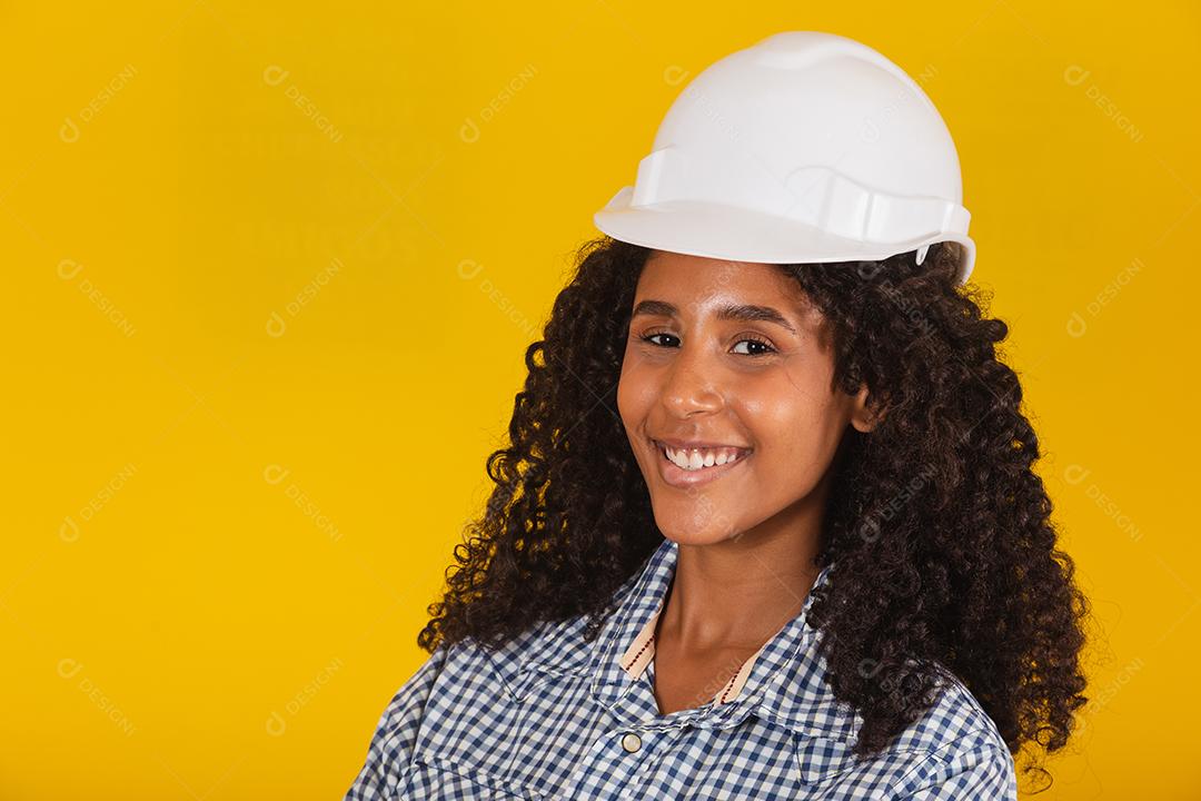 Engenheira ou arquiteta em fundo amarelo sorrindo com os braços cruzados.
