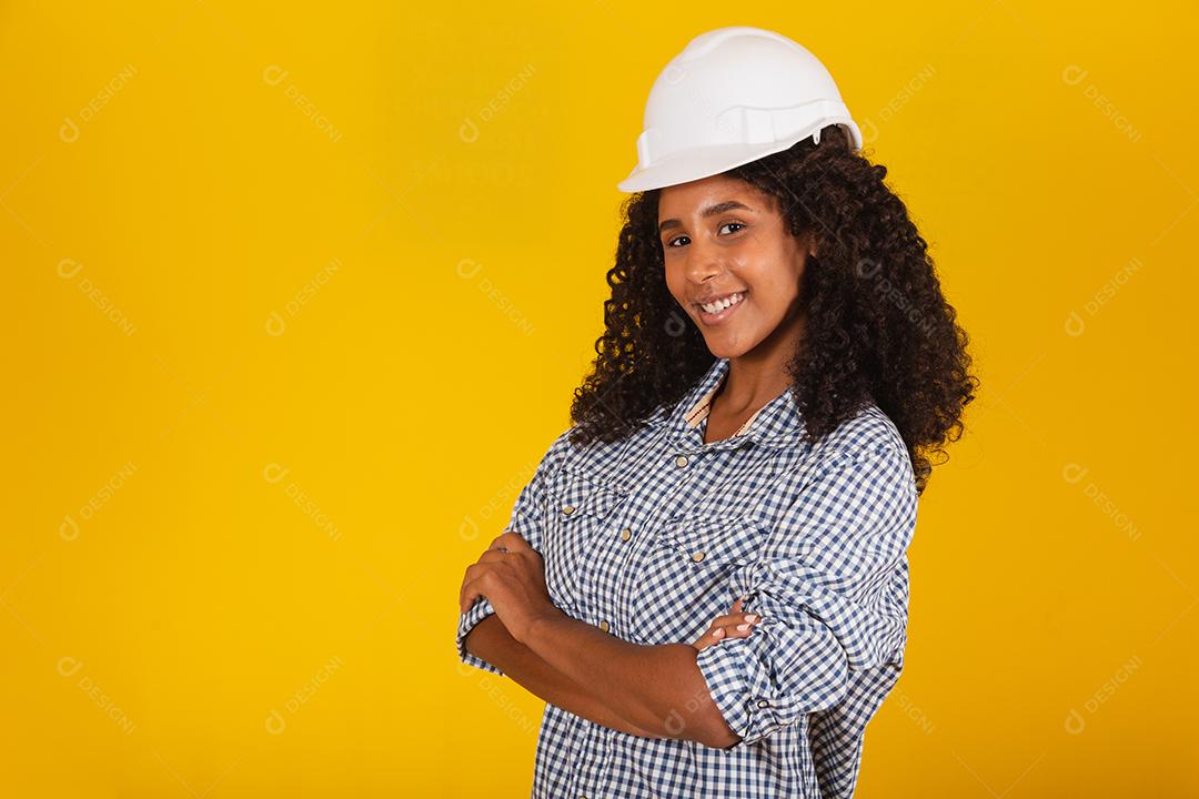 Engenheira ou arquiteta em fundo amarelo sorrindo com os braços cruzados.