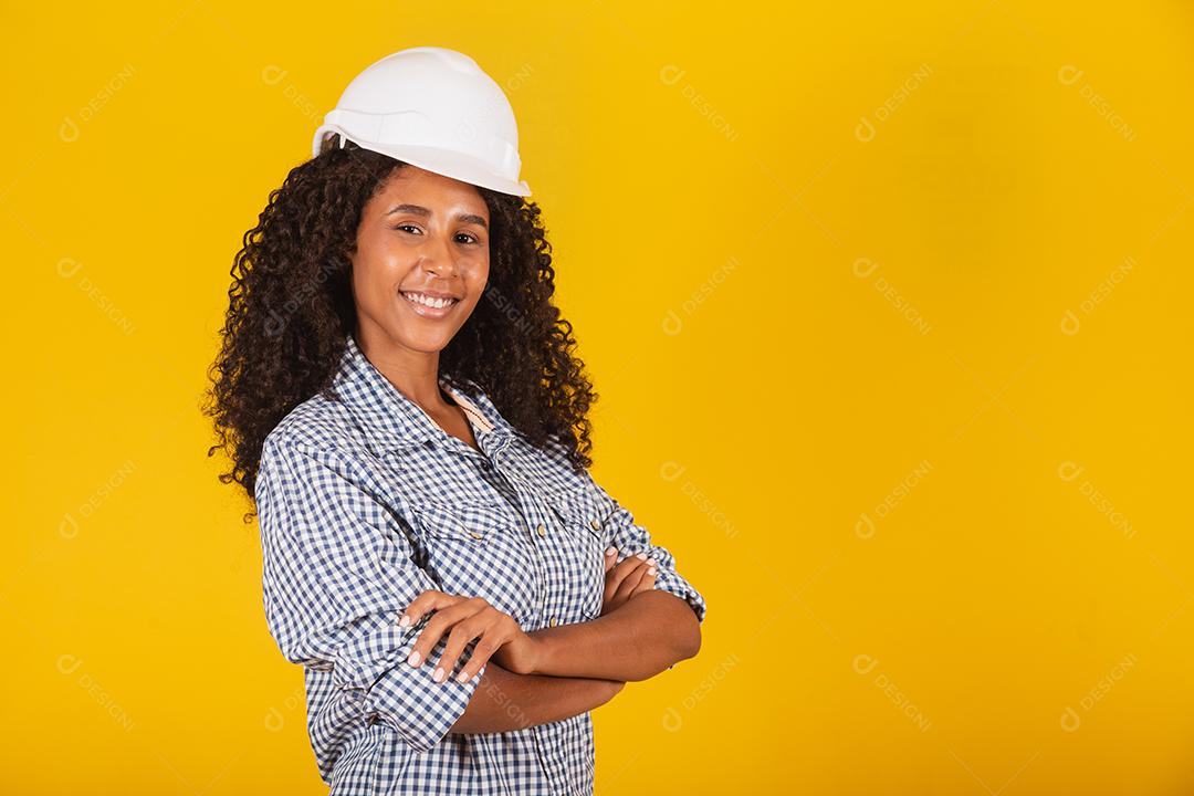 Engenheira ou arquiteta em fundo amarelo sorrindo com os braços cruzados.