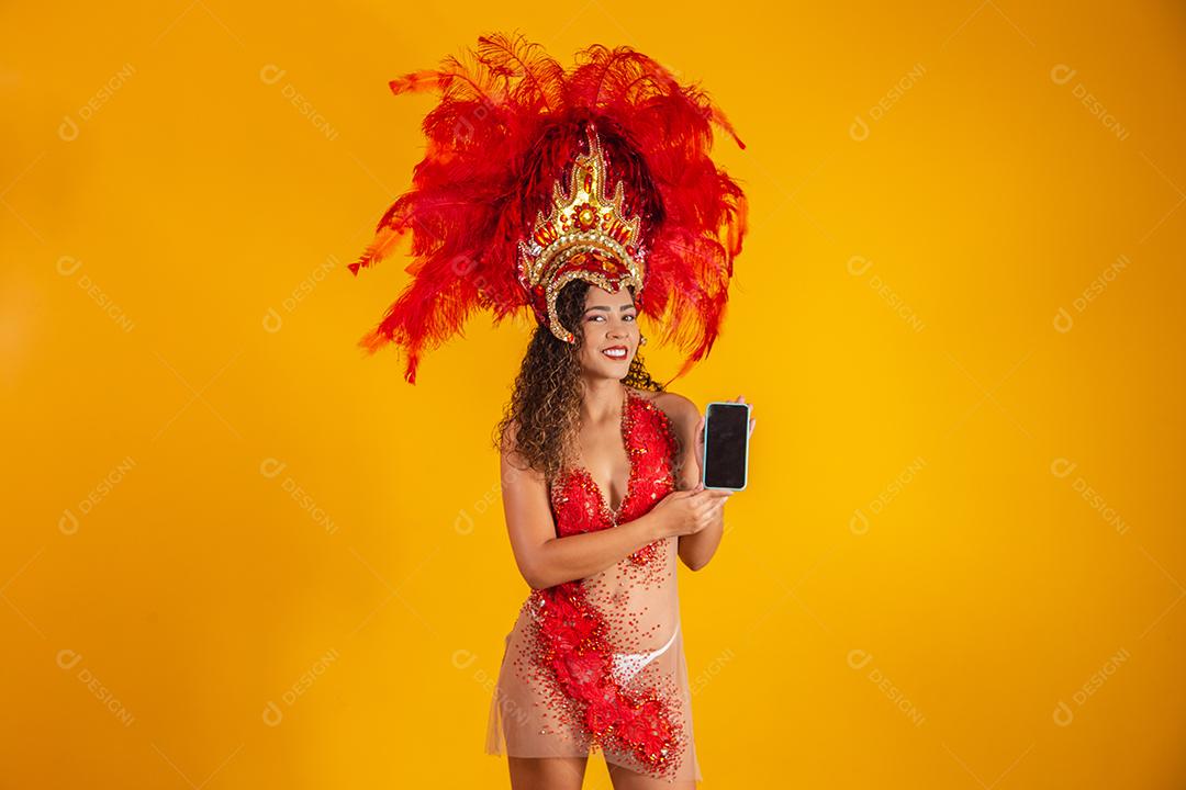 Mulher jovem e bonita em traje especial de penas de carnaval segurando um smartphone com tela em branco