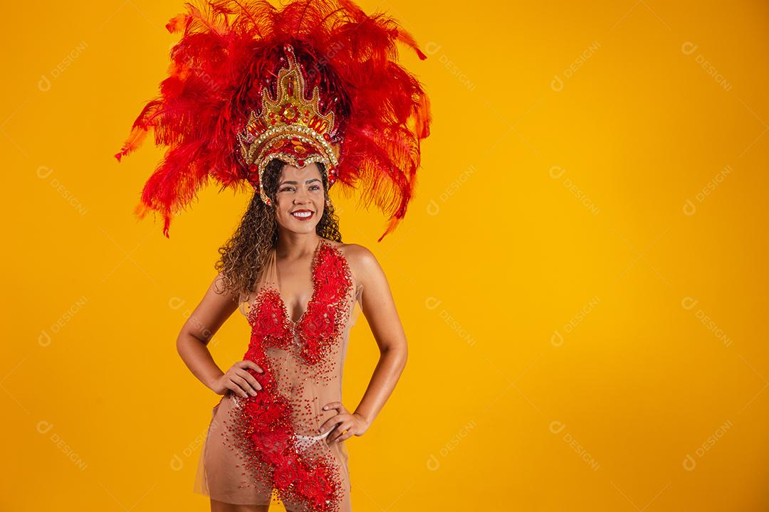 Mulher afro brasileira posando em traje de samba sobre fundo amarelo com espaço livre. Traje brasileiro de samba vestido.