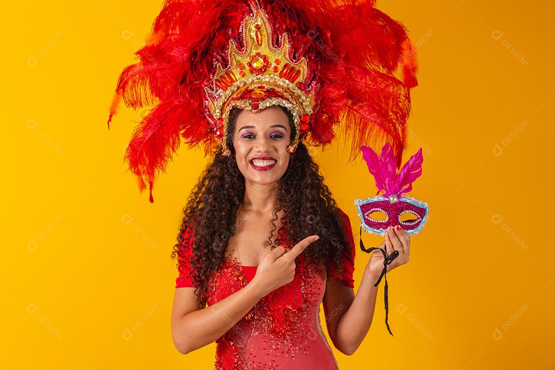 Jovem afro com roupa de samba e carnaval segurando uma máscara rosa.