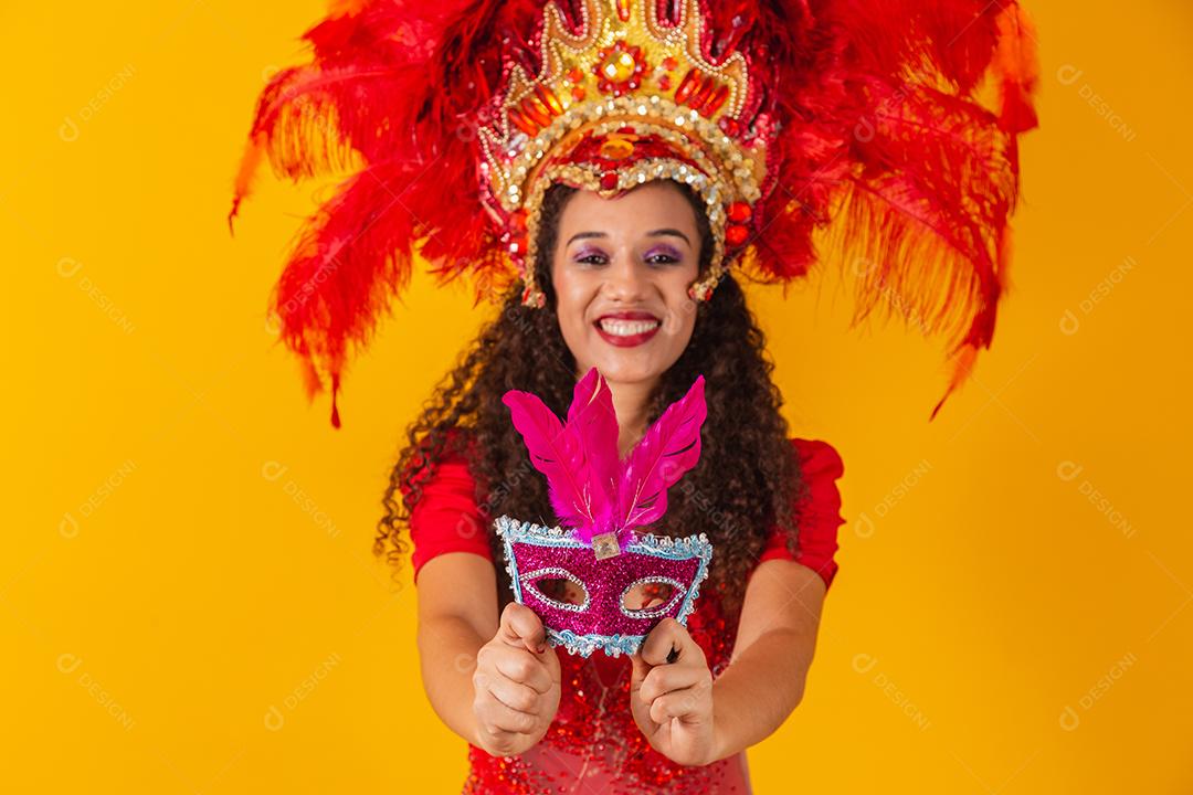 Jovem afro com roupa de samba e carnaval segurando uma máscara rosa.