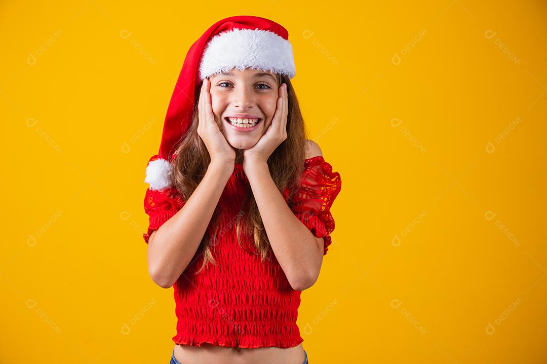 Retrato de uma menina sorridente caucasiana com um chapéu de Papai Noel em um fundo amarelo