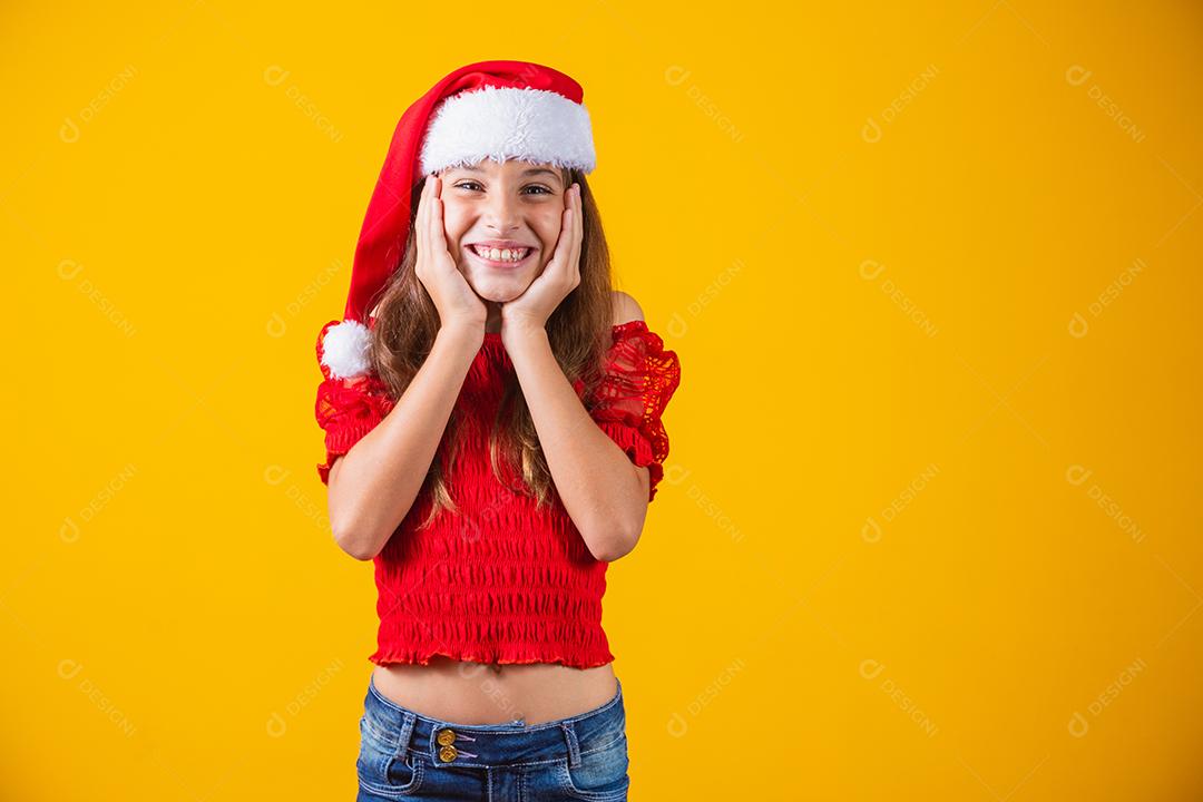 Retrato de uma menina sorridente caucasiana com um chapéu de Papai Noel em um fundo amarelo