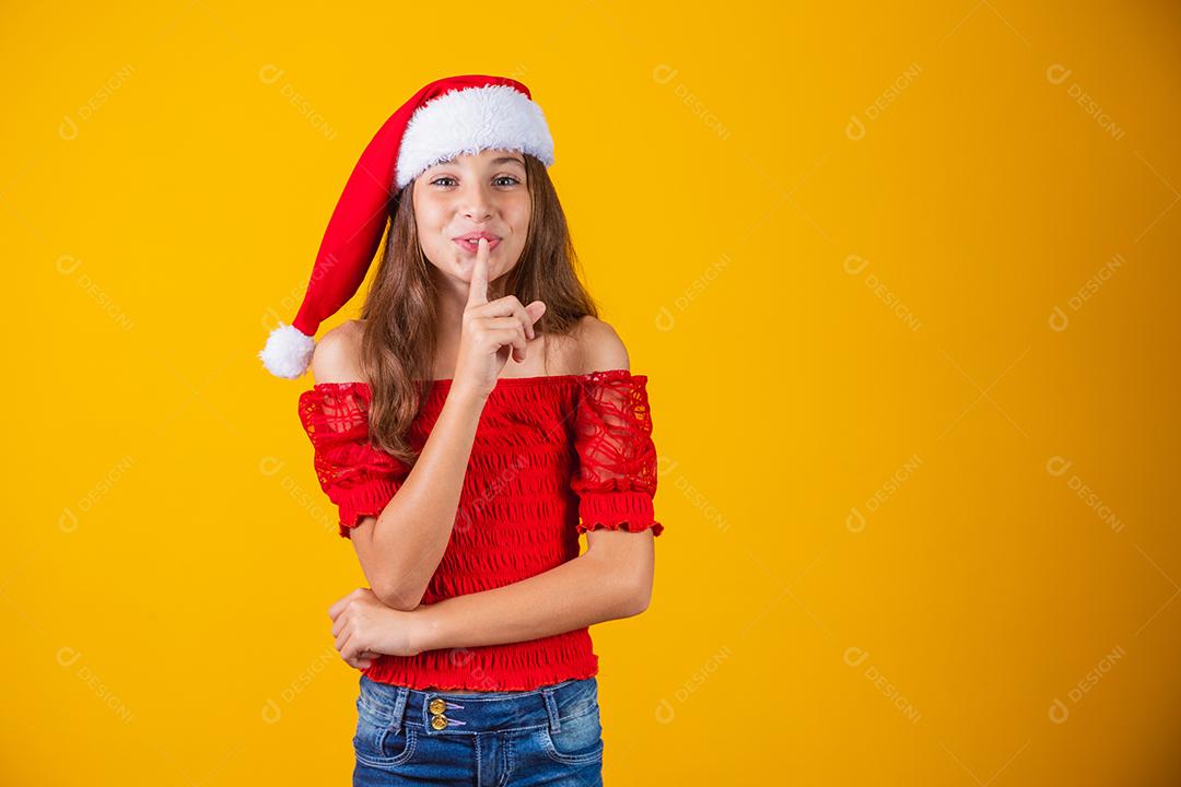 menina vestida para o natal fazendo sinal de silêncio em fundo amarelo.