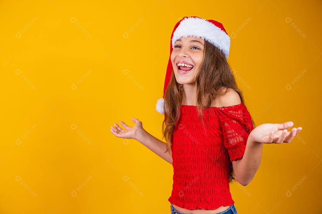 menina vestida para o natal encantada com a boca aberta sobre fundo amarelo.