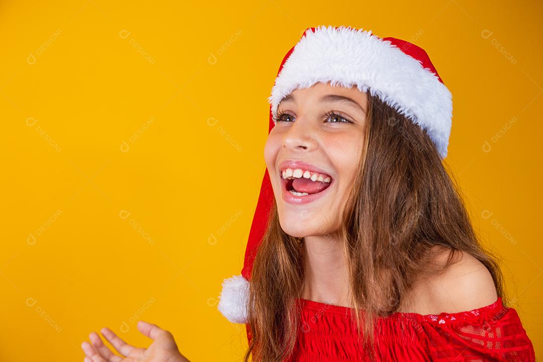 menina vestida para o natal encantada com a boca aberta sobre fundo amarelo.