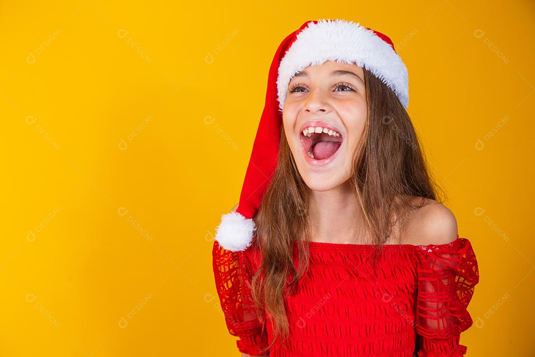 menina vestida para o natal encantada com a boca aberta sobre fundo amarelo.