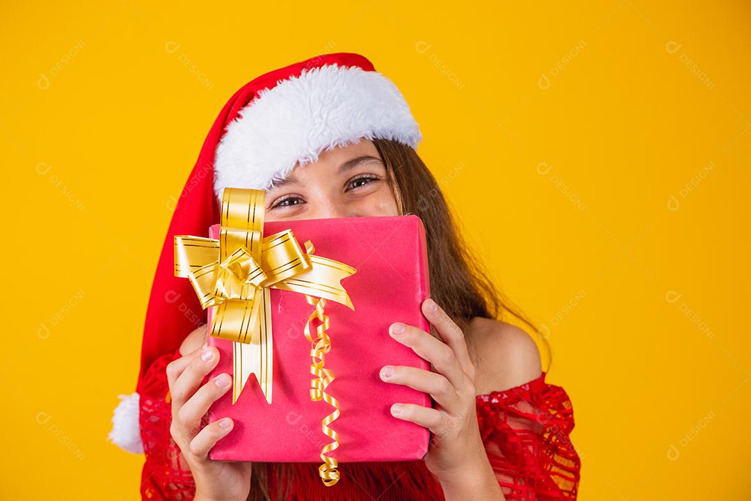 Alegre sorridente criança engraçada no chapéu de papai noel vermelho segurando o presente de natal