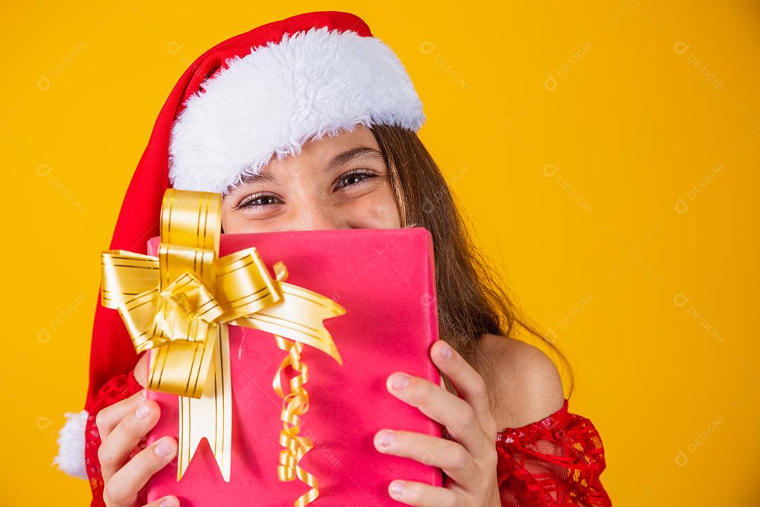 Alegre sorridente criança engraçada no chapéu de papai noel vermelho segurando o presente de natal