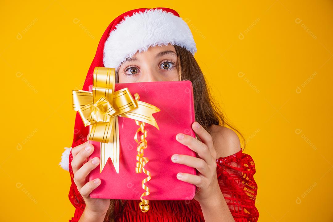 Alegre sorridente criança engraçada no chapéu de papai noel vermelho segurando o presente de natal