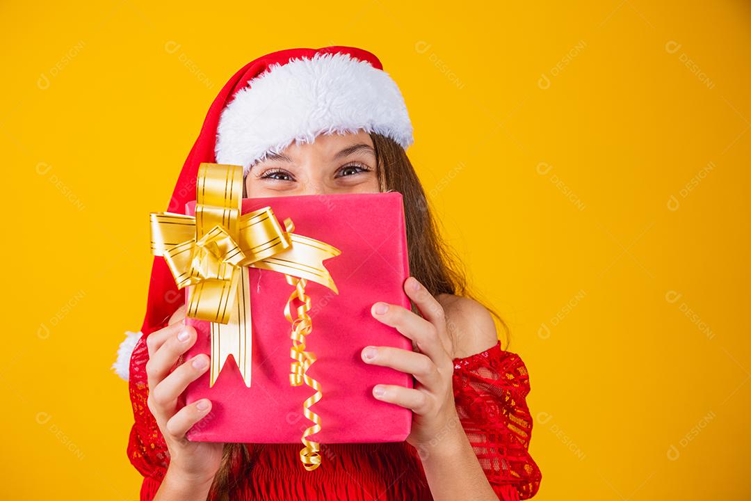 Alegre sorridente criança engraçada no chapéu de papai noel vermelho segurando o presente de natal