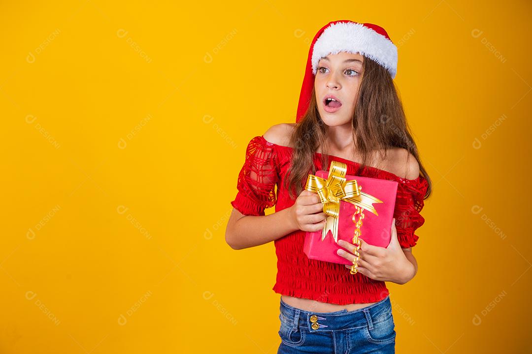 linda garota alegre com um chapéu de Natal em um fundo colorido segurando um presente