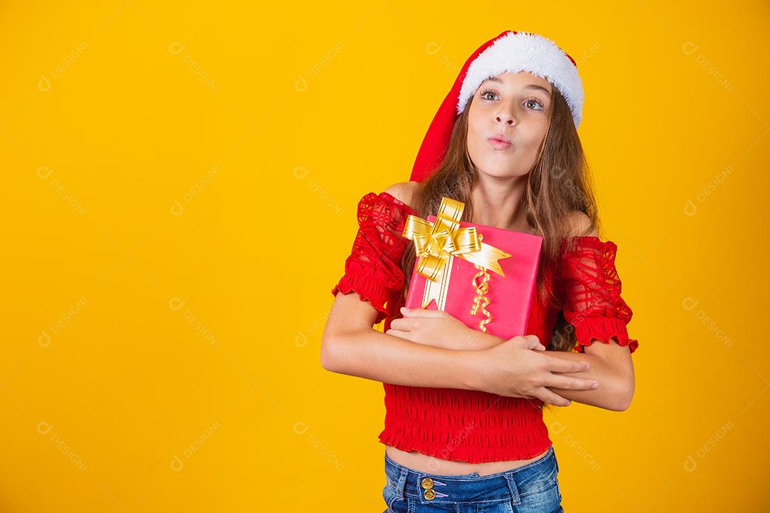 linda garota alegre com um chapéu de Natal em um fundo colorido segurando um presente