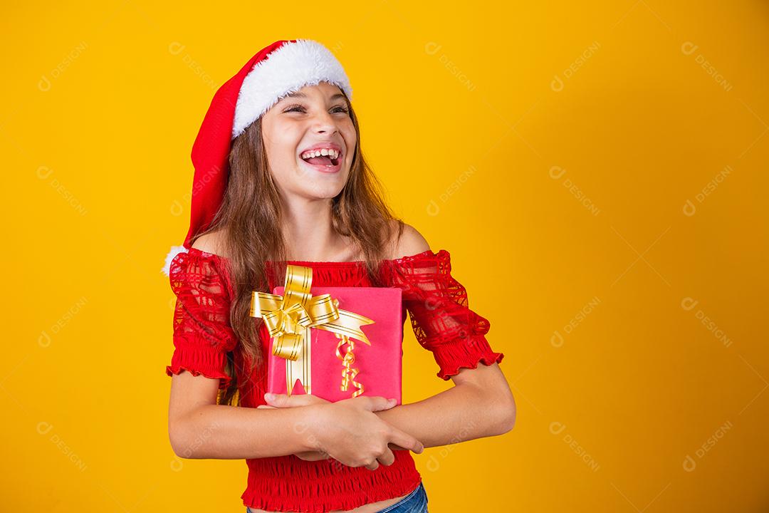 linda garota alegre com um chapéu de Natal em um fundo colorido segurando um presente